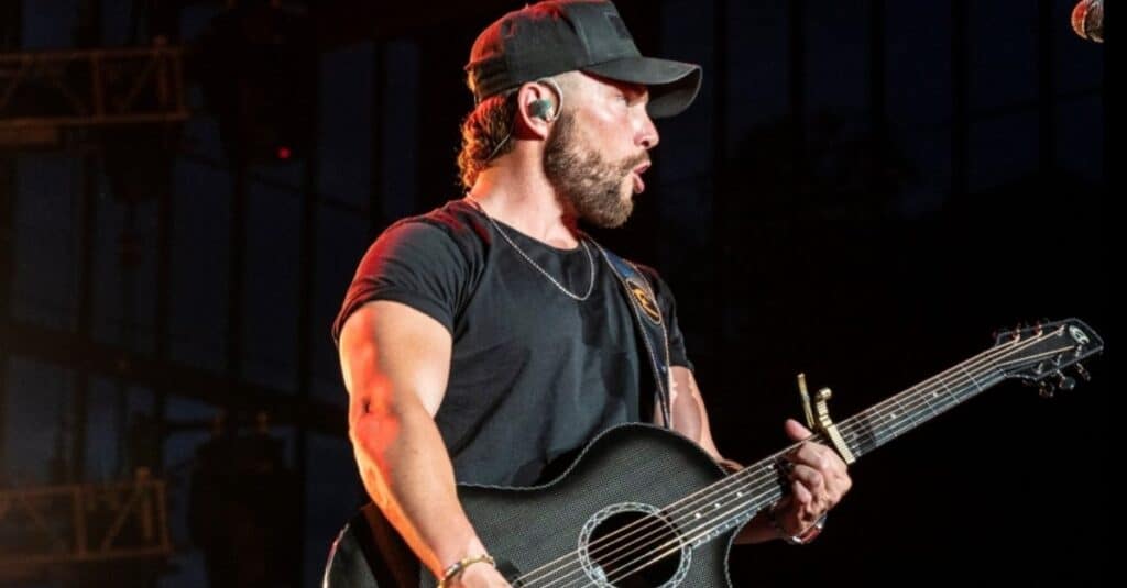 Chris Lane  in a hat, passionately plays an acoustic guitar, creating a captivating musical atmosphere.