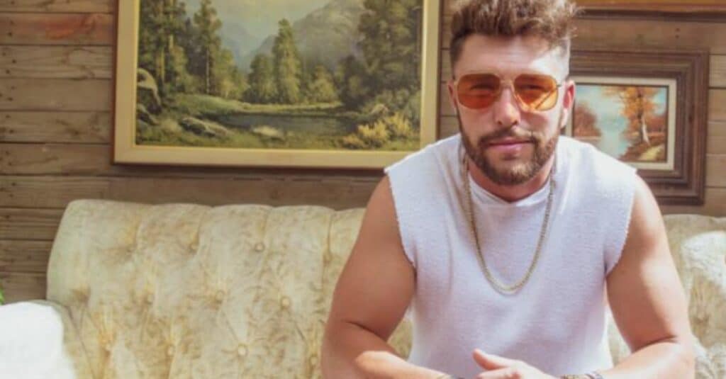 Chris Lane wearing sunglasses, relaxed on a couch, exuding a casual and stylish vibe.