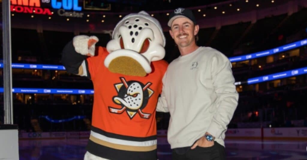 Jake Knapp poses next to a playful duck mascot at an ice rink, capturing a moment of joy and excitement.