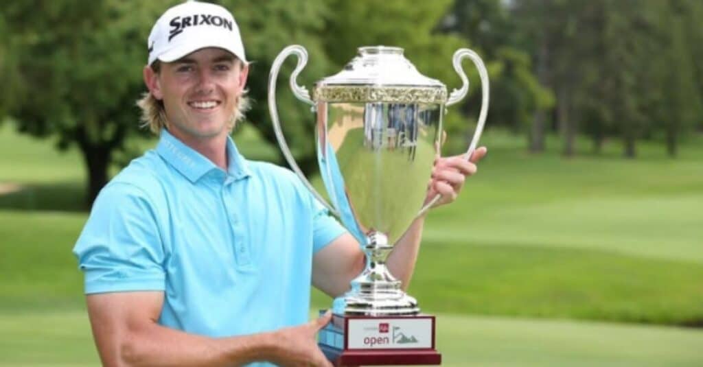 Jake Knapp stands on a golf course, holding a trophy aloft, symbolizing his recent achievement.