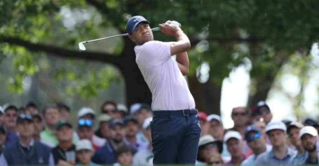 Tony Finau, dressed in a pink shirt, is captured mid-swing with his golf club, demonstrating skill and concentration.