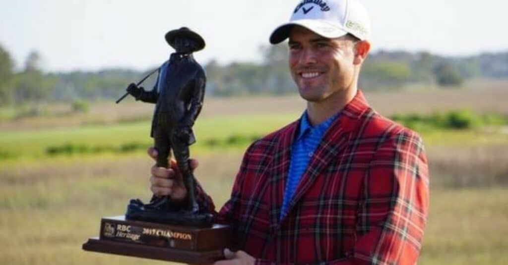 Wesley Bryan, dressed in a plaid jacket, stands confidently while holding a trophy, symbolizing his victory.