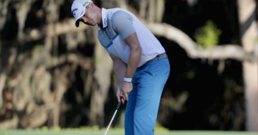 Wesley Bryan, dressed in blue pants and is focused on making a putt on the golf course.