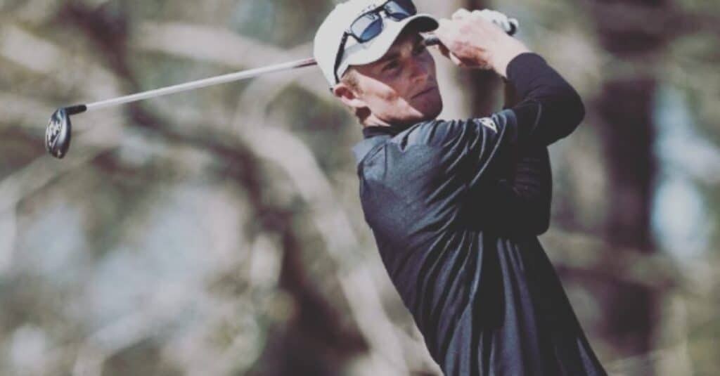 A man in a black shirt and sunglasses, Will Zalatoris, is focused on playing golf on a sunny day.