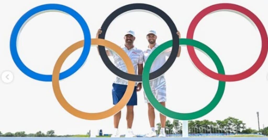 Wyndham Clark and another man pose in front of the large Olympic rings, representing the spirit of international competition.