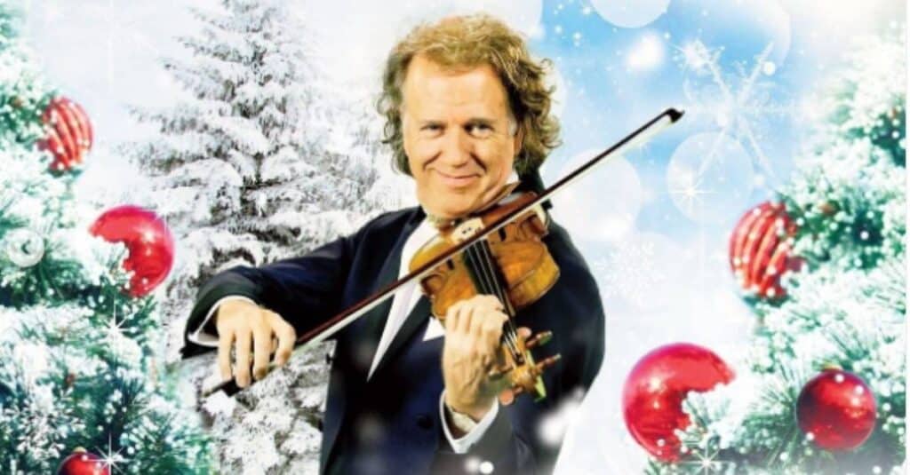 Andre Rieu, dressed in a tuxedo, performs on the violin surrounded by elegant Christmas decorations.