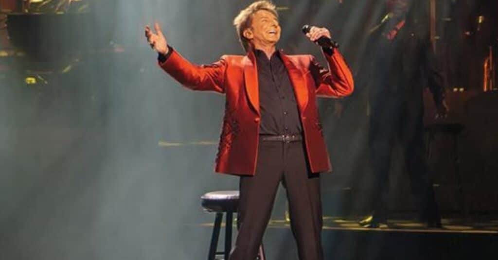 Barry Manilow in a red suit passionately singing on stage, reminiscent of Barry Manilow's iconic performances.