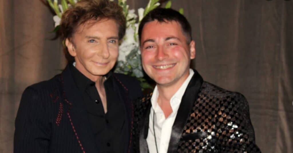 Barry Manilow and another man smiling together, posing for a cheerful photograph.