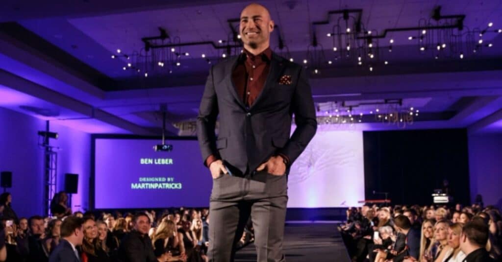 Ben Leber, dressed in a suit and tie, stands on a stage, showcasing elegance and poise in a professional setting.