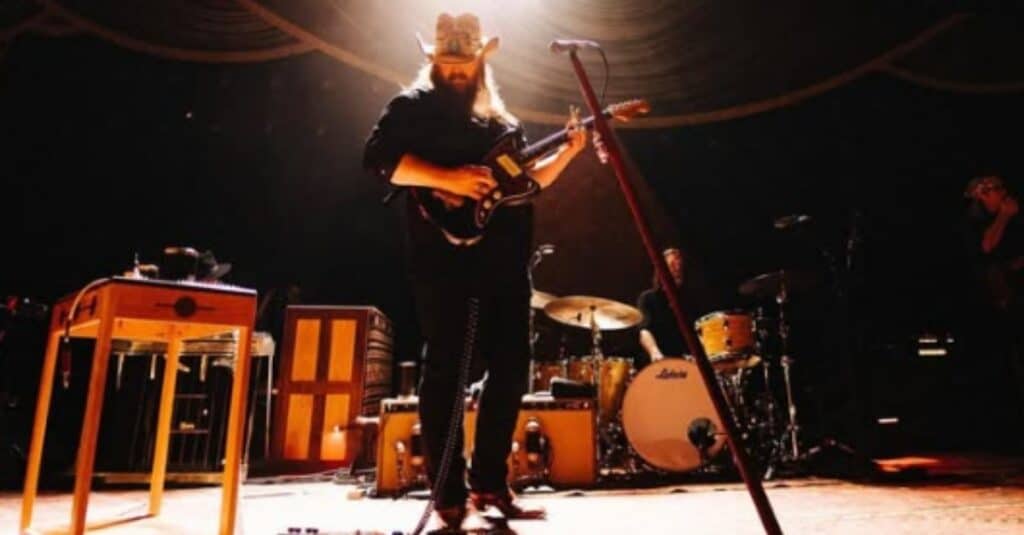 Chris Stapleton, wearing a hat, captivates the audience with his guitar performance on stage.