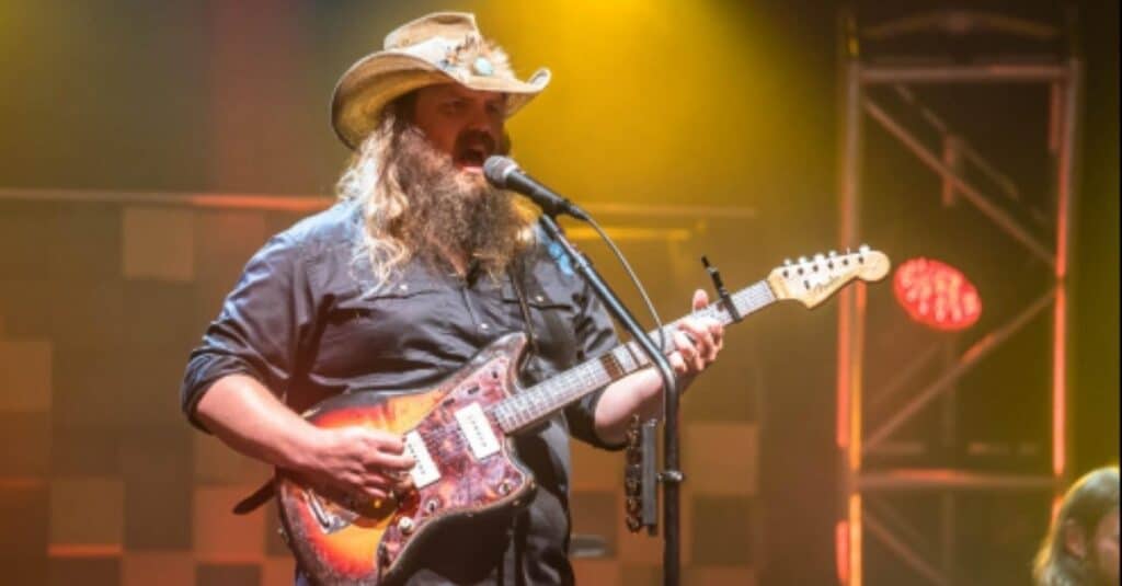 Chris Stapleton  in a hat skillfully strumming a guitar, capturing the essence of Chris Stapleton's artistry.