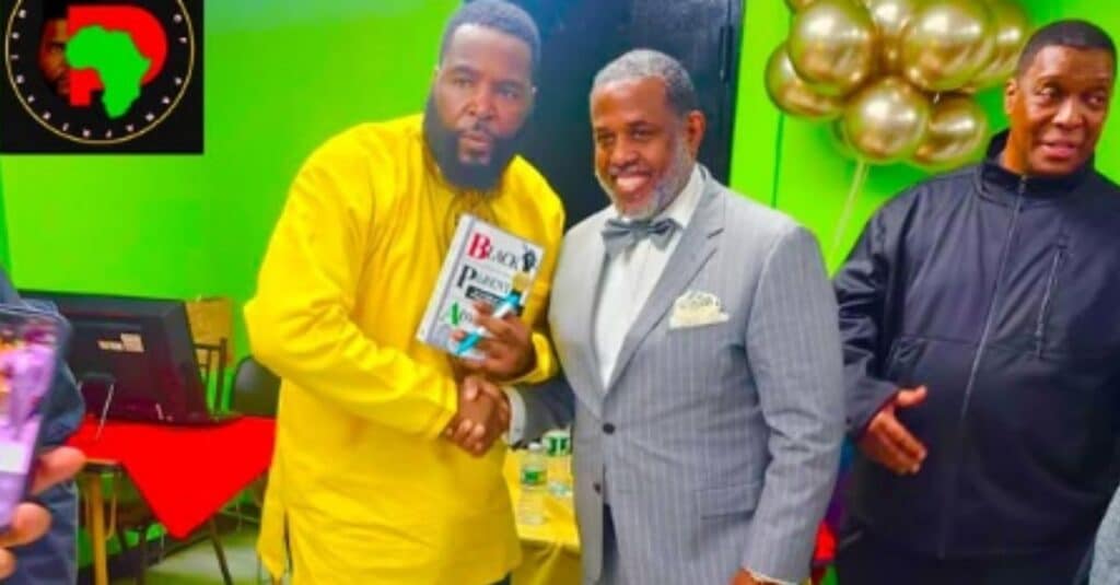 Dr. Umar Johnson stands next to another man, who is holding a book, both engaged in a thoughtful discussion.