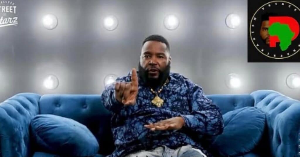 Dr. Umar Johnson is seated on a couch, with his hands raised, conveying a message or engaging in discussion.