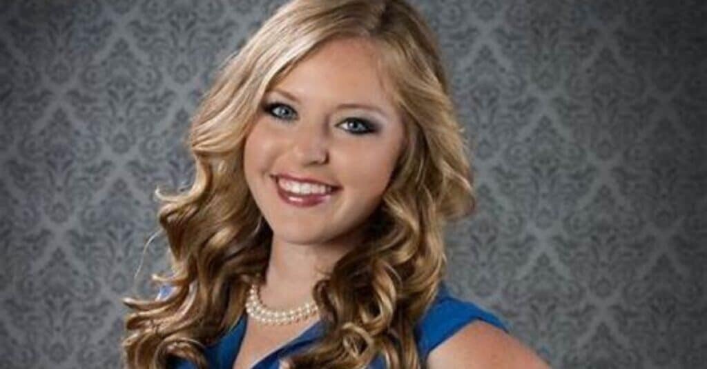 Emily Mae Young, a stunning young woman in a blue dress, showcasing her long hair and captivating presence.