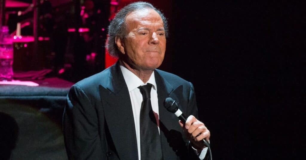 Julio Iglesias, dressed in a suit and tie, stands confidently with a microphone in hand, poised for a performance.