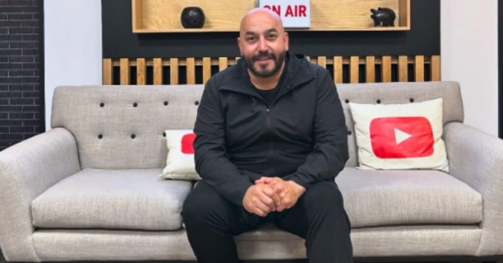 Lupillo Rivera relaxes on a couch adorned with the YouTube logo, showcasing a casual atmosphere.